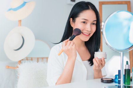 Beautiful asian woman blogger is showing how to make up and use cosmetics. In front of the mirror and smartphone recording vlog video live streaming at home.Skincare for healthy face concept.の写真素材