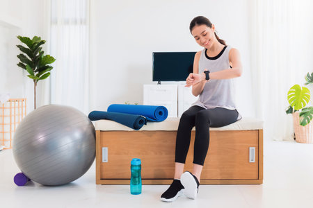 Asian woman resting and using smart watch after play yoga and exercise at home background with copy space.Concept of sport technology to checking health data.の写真素材