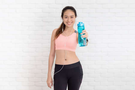 Asian beautiful women holding water bottle after play yoga and exercise on white brick wall...