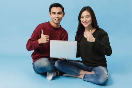 Asian young couple sitting and using laptop with smiling face together isolated on blue...