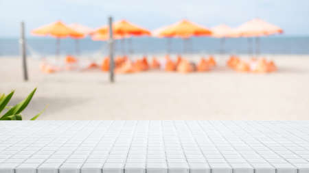 Empty white ceramic mosaic table top and blurred sand beach by the sea in tropical resort.Summer banner background - can used for display or montage your products.の写真素材