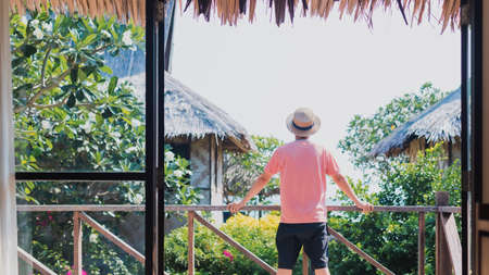 Traveller man standing at balcony of wooden house by the sea with tropical tree background.Beautiful landscape for travel.の写真素材