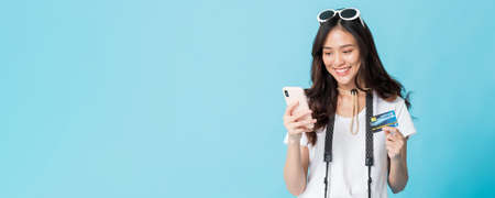 Asian pretty woman tourist preparing for travel and shopping online with smartphone and credit card isolated on blue banner background.Concept of people using technology of travel.の写真素材