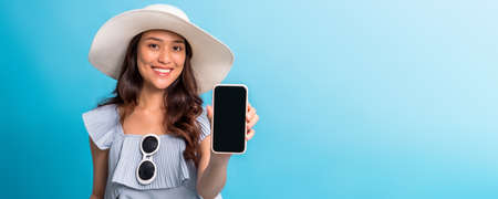 Asian pretty woman tourist preparing for travel showing smartphone screen to copy space isolated on blue banner background.の写真素材