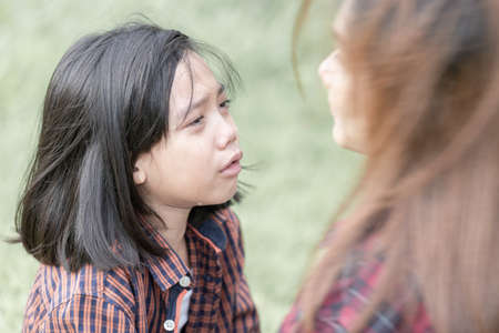 Mother looking at crying daughter, girl crying with tears in parkの写真素材