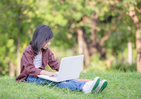 Girl sitting on the grass studying with laptop in the park, Outdoor learning concept