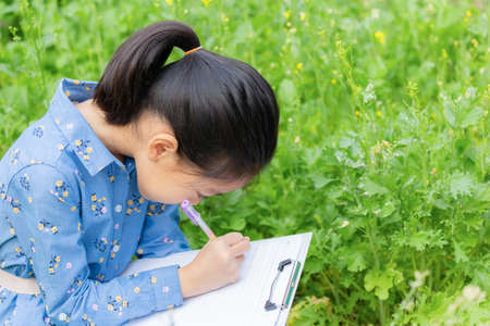 Little cute girl checking vegetable and writing record document in a farm, Learning outside the...