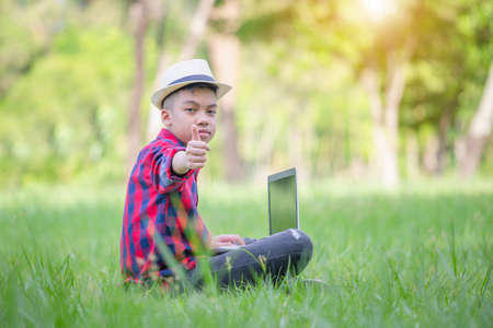 Boy giving thumbs up and sitting on the grass studying with laptop in the park, Outdoor learning...