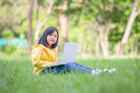 Smiling girl sitting on the grass studying with laptop in the park, Outdoor learning conceptの写真素材