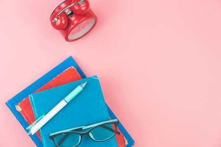 Top view with copy space of books, glasses, pen and clocks overhead on pink pastel background, Flat lay and education conceptの写真素材