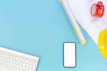 Top view with copy space of Engineering tools, computer keyboard, smartphone, blueprints, helmet, measuring tape overhead on blue pastel background, Flat lay conceptの写真素材