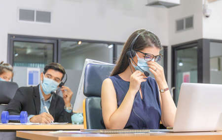 Young telephone operator with headset wear protection face mask against coronavirus, Customer service executive team working at officeの写真素材