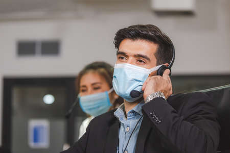 Young telephone operator with headset wear protection face mask against coronavirus, Customer...