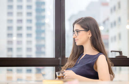 Relaxing young businesswoman sitting and looking away with while drinking teaの写真素材