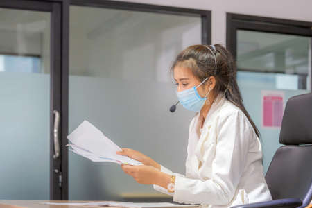 Young woman telephone operator with headset wear protection face mask against coronavirus, Customer service executive team working at officeの写真素材