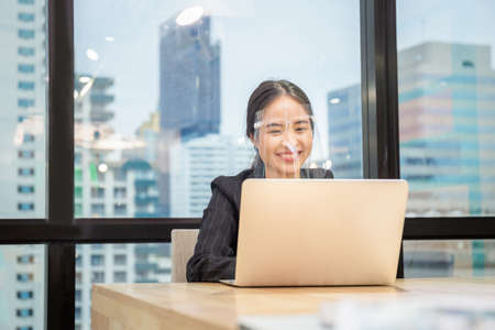 Cheerful businesswoman wearing face shield and video conference calling on laptop computer, New normal conceptの写真素材