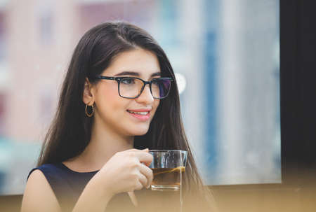 Cheerful and relaxing young businesswoman sitting and looking away with while drinking tea