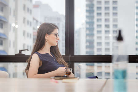 Relaxing young businesswoman sitting and looking away with while drinking tea, Business office new normal conceptの写真素材