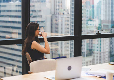Relaxing young businesswoman sitting and looking away with while drinking teaの写真素材