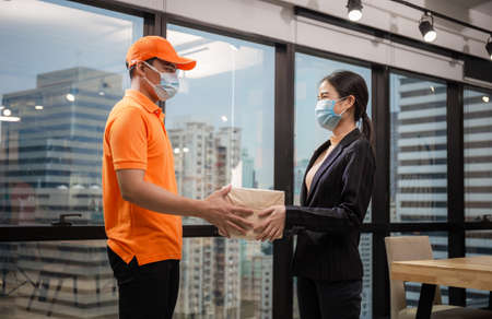 Woman wear face mask receiving parcel from delivery service, Young delivery man employee in t-shirt uniform wear face maskの写真素材
