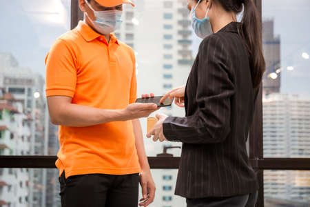 Woman signing on device to delivery parcel, Young delivery man employee in t-shirt uniform wear face maskの写真素材
