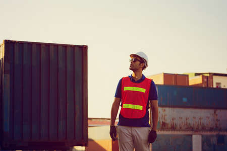 Factory worker in hardhat and safety vest holding two-way radio control loading containers box from cargoの写真素材