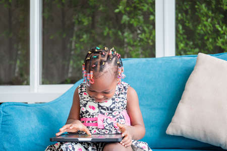 Cheerful african american girl playing on tablet in the living roomの写真素材