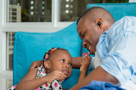 Cheerful african american father and daughter playing in living room, Cute little girl enjoying with chocolate, Happiness family conceptsの写真素材