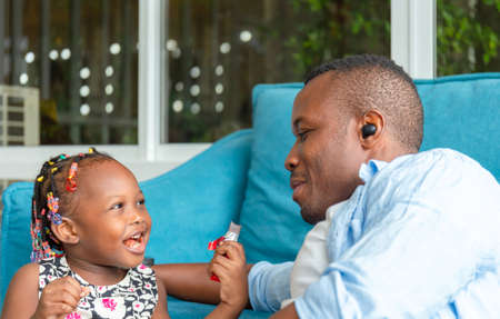 Cheerful african american father and daughter playing in living room, Cute little girl enjoying with chocolate, Happiness family conceptsの写真素材