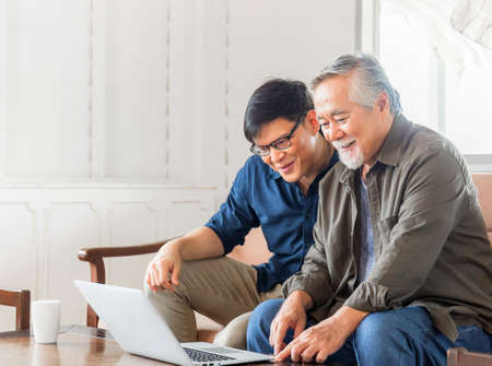 Happiness senior asian father and adult son using laptop talking on video call in living roomの写真素材