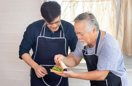 Cheerful senior asian father and middle aged son cooking together at kitchenの写真素材