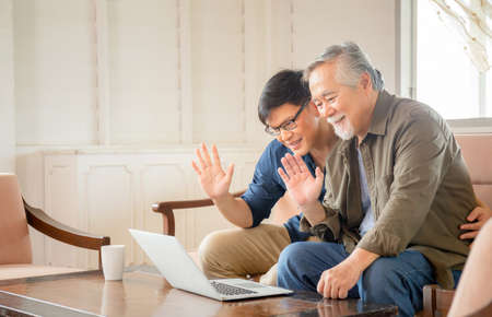 Elderly and technology concept, Happiness senior asian father and adult son using laptop talking on video call in living roomの写真素材