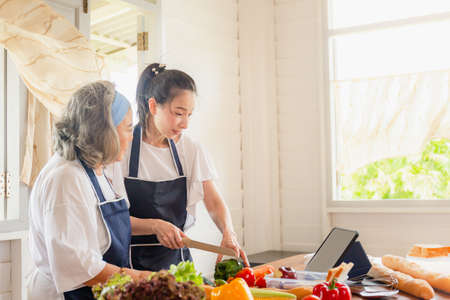 Senior asian mother and middle aged daughter cooking together at kitchenの写真素材