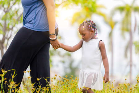 African american mother holding hand of her daughter walking in the parkの写真素材