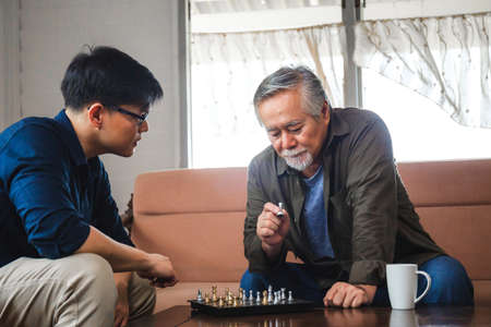 Senior asian father and middle aged son playing chess game in living room, Happiness Asian family...