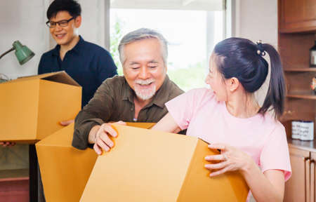 Moving day concepts, Asian family carrying boxes into new home, Happiness middle aged daughter son and senior father in new houseの写真素材