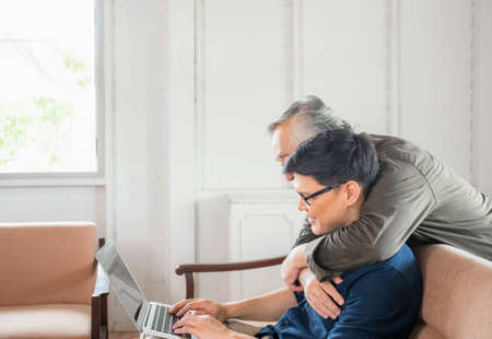 Happy senior asian father and adult son using laptop talking on video call in living roomの写真素材