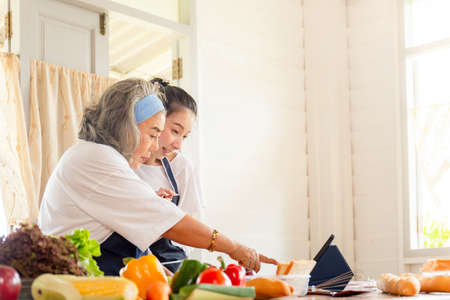 Senior asian mother and middle aged daughter cooking together at kitchen