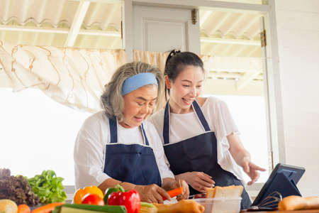 Senior asian mother and middle aged daughter cooking together at kitchenの写真素材