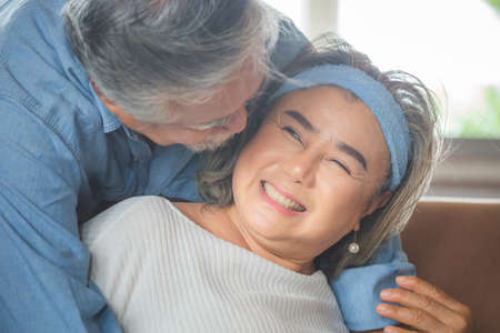 Close up portrait of happy senior asian couple hugging in living roomの写真素材