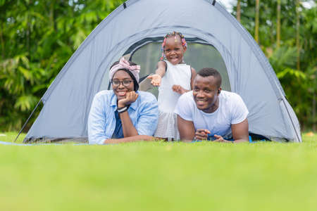 Cheerful african american family enjoying in the park, Mother father and daughter playing camping at outdoor, Happiness family conceptsの写真素材