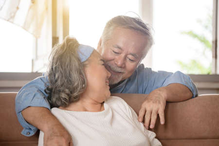 Close up portrait of happy senior asian couple hugging in living roomの写真素材