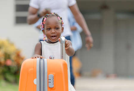 Travel concepts, Orange luggage with blurred cheerful african american girl and parent family leaving house for vacationの写真素材