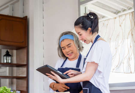 Senior asian mother and middle aged daughter cooking together at kitchenの写真素材