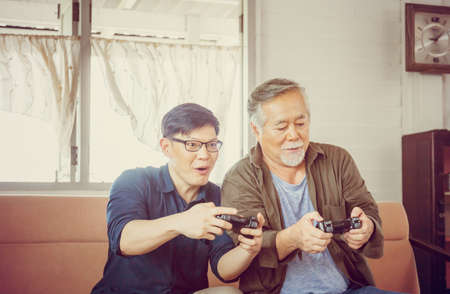 Happy Senior asian father and middle aged son playing video game together in living room, Happiness Asian family conceptsの写真素材