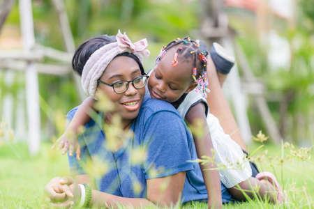African american girl playing on the back of her mother, Happy mother and daughter laughing together outdoorの写真素材
