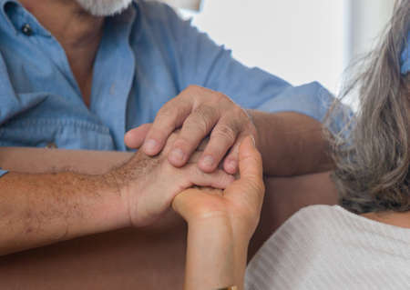Elderly asian couple holding hands while sitting together in living room at home, Happiness family conceptsの写真素材