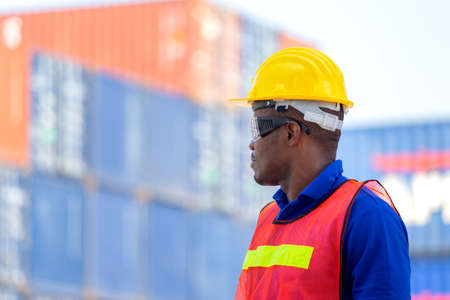 Worker man in hardhat and safety vest standing at containers cargo, Foreman control loading containers box from cargoの写真素材
