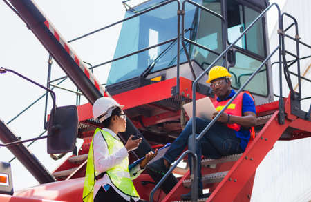 Female foreman safety vest using clipboard checklist and Worker man in hardhat holding laptop for control loading containers box from cargoの写真素材