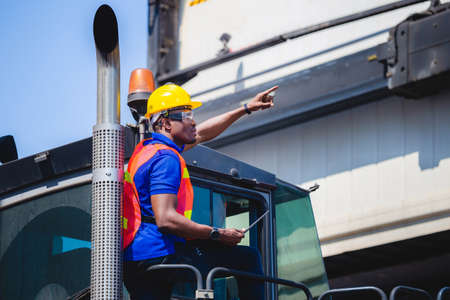 Worker man in hardhat and safety vest holding laptop standing on container stackers control loading containers box from cargoの写真素材